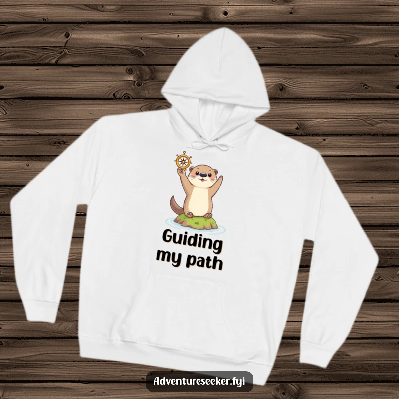 Funny Otter Hoodie: Curious otter triumphantly holding a tiny compass aloft on a small island, warm and guided.